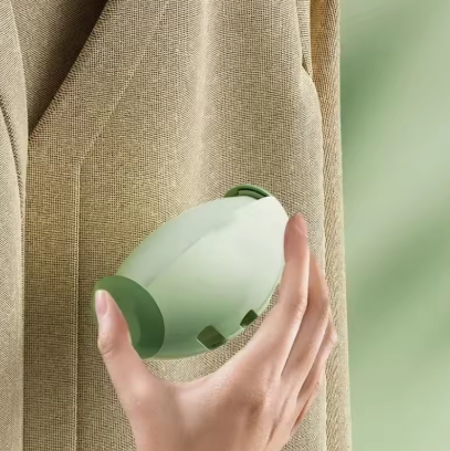 Hand holding a green and white Portable Pet Hair Roller against a textured beige background
